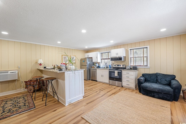 kitchen featuring a sink, a breakfast bar, light wood finished floors, a peninsula, and appliances with stainless steel finishes