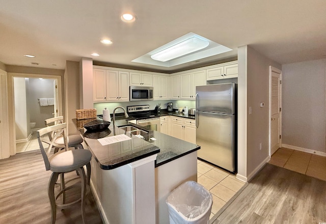 kitchen with a kitchen breakfast bar, recessed lighting, a sink, stainless steel appliances, and light wood finished floors
