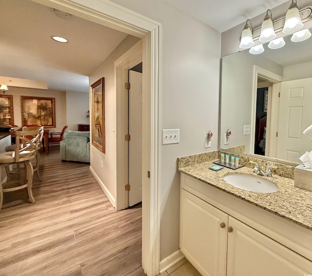 bathroom with recessed lighting, vanity, baseboards, and wood finished floors