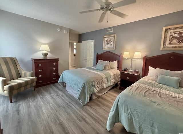 bedroom featuring a textured ceiling, wood finished floors, ceiling fan, and visible vents