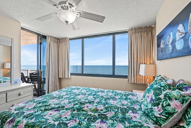 bedroom featuring a water view, access to exterior, multiple windows, and a textured ceiling