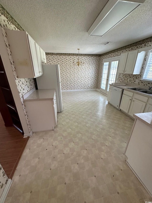 kitchen featuring a sink, a textured ceiling, wallpapered walls, white appliances, and light countertops