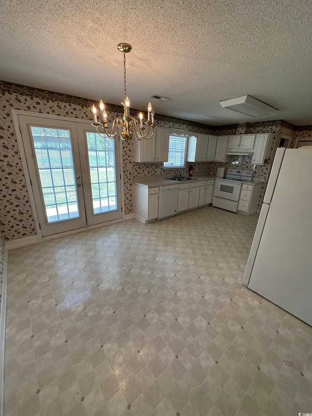 kitchen featuring wallpapered walls, an inviting chandelier, a textured ceiling, and white appliances