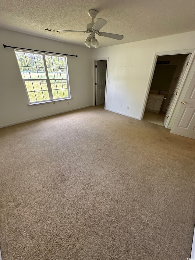 unfurnished bedroom featuring carpet floors, a textured ceiling, ensuite bathroom, and baseboards