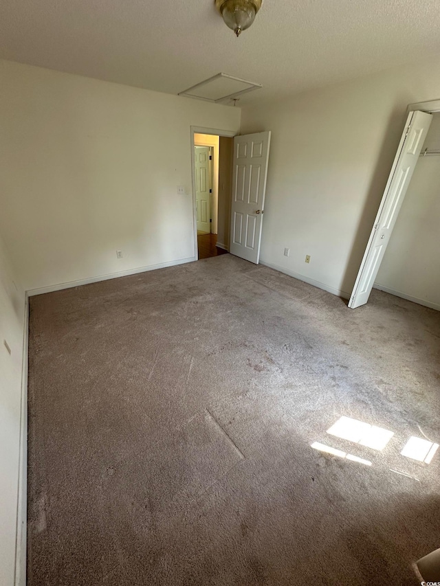 unfurnished room featuring attic access, carpet floors, and baseboards