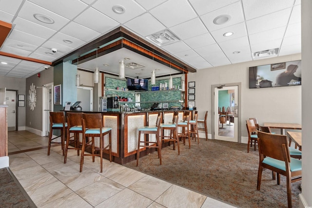 bar with visible vents, carpet flooring, a drop ceiling, and baseboards