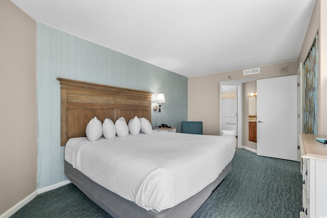 bedroom with baseboards, visible vents, dark carpet, and ensuite bath