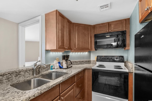 kitchen featuring light stone counters, brown cabinets, black appliances, a sink, and visible vents