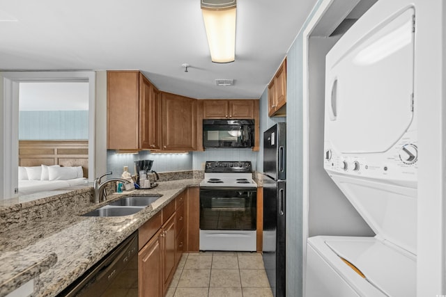 kitchen with brown cabinets, a sink, stacked washer / drying machine, visible vents, and black appliances