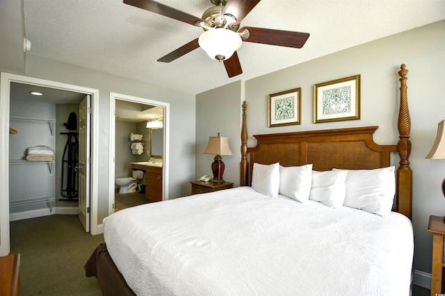 carpeted bedroom featuring baseboards, a spacious closet, a textured ceiling, a ceiling fan, and connected bathroom
