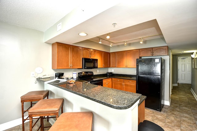 kitchen featuring brown cabinetry, a peninsula, baseboards, and black appliances