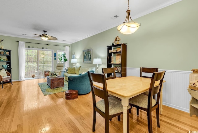dining area featuring light wood-type flooring, a ceiling fan, wainscoting, and ornamental molding