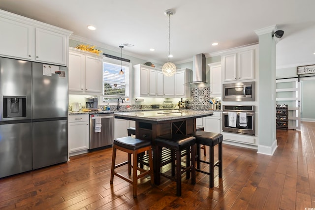 kitchen with stainless steel appliances, a kitchen island, wall chimney range hood, ornamental molding, and dark wood-type flooring
