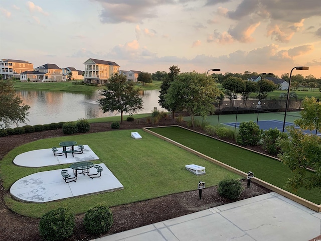 view of property's community with fence, a lawn, and a water view