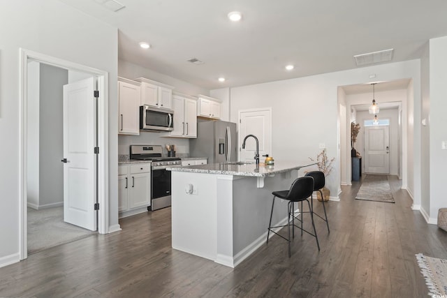 kitchen with stainless steel appliances, a sink, dark wood finished floors, a kitchen island with sink, and recessed lighting