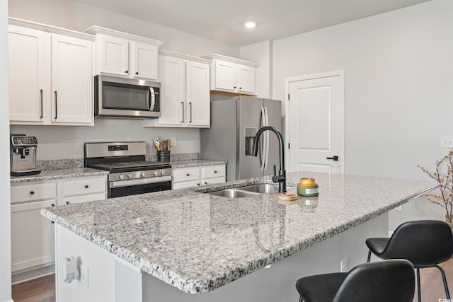 kitchen featuring appliances with stainless steel finishes, a sink, white cabinets, a kitchen island with sink, and a kitchen bar