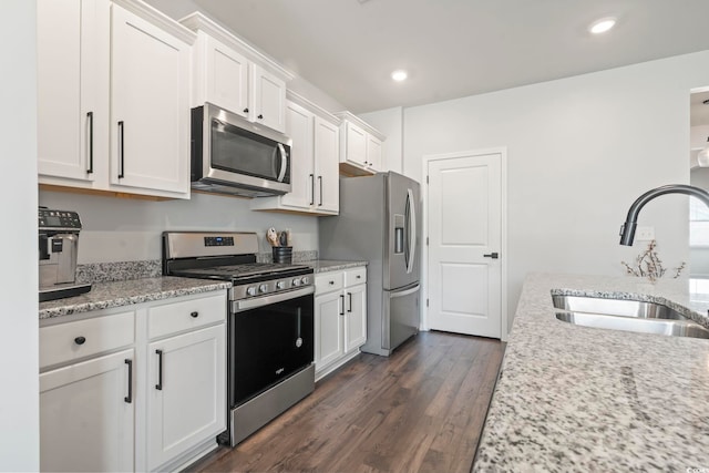 kitchen featuring stainless steel appliances, a sink, white cabinetry, dark wood-style floors, and light stone counters