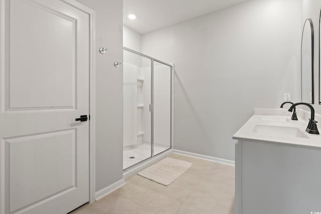 bathroom featuring a stall shower, baseboards, tile patterned floors, and double vanity