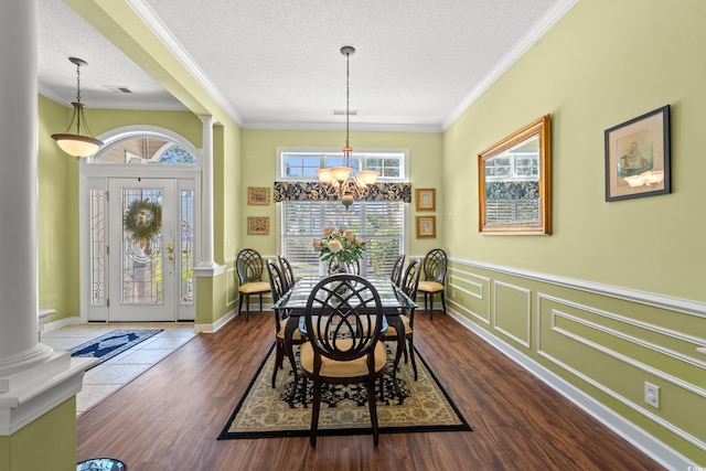 dining area featuring decorative columns, a textured ceiling, crown molding, dark wood finished floors, and a notable chandelier