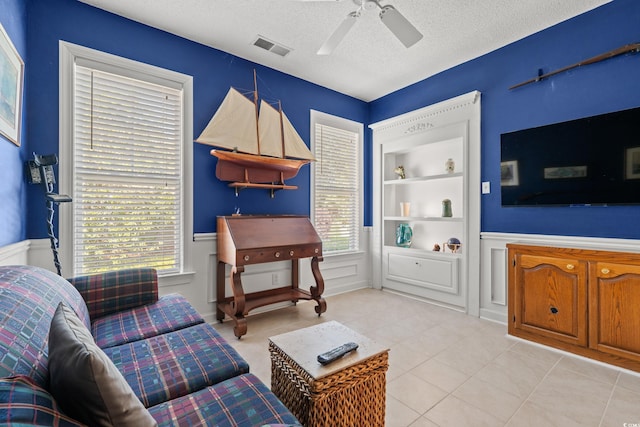 living room featuring ceiling fan, a textured ceiling, visible vents, wainscoting, and built in shelves