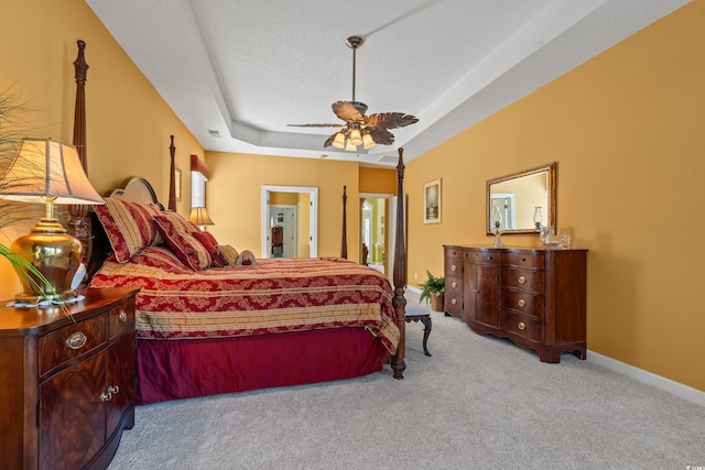 carpeted bedroom featuring a ceiling fan, a textured ceiling, visible vents, baseboards, and a tray ceiling