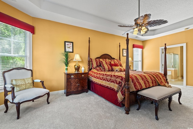 carpeted bedroom with baseboards, connected bathroom, a textured ceiling, a tray ceiling, and a ceiling fan