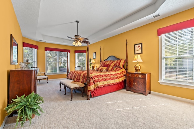 carpeted bedroom featuring baseboards, ceiling fan, and a tray ceiling