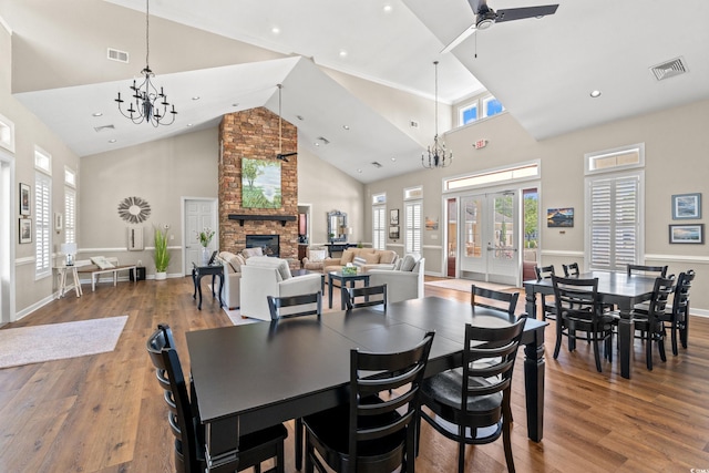 dining room with a large fireplace, high vaulted ceiling, wood finished floors, and visible vents