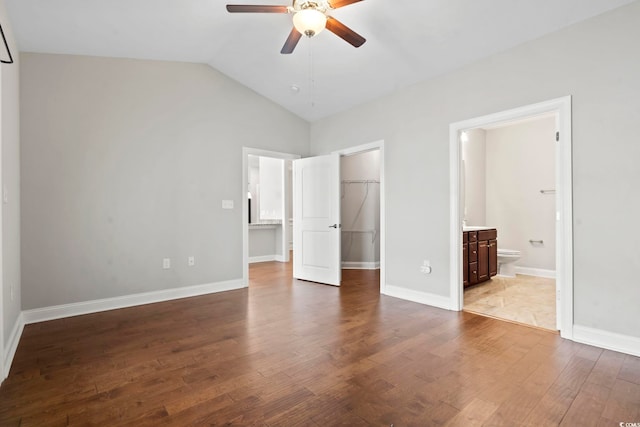 unfurnished bedroom featuring a spacious closet, wood finished floors, lofted ceiling, a closet, and ensuite bath