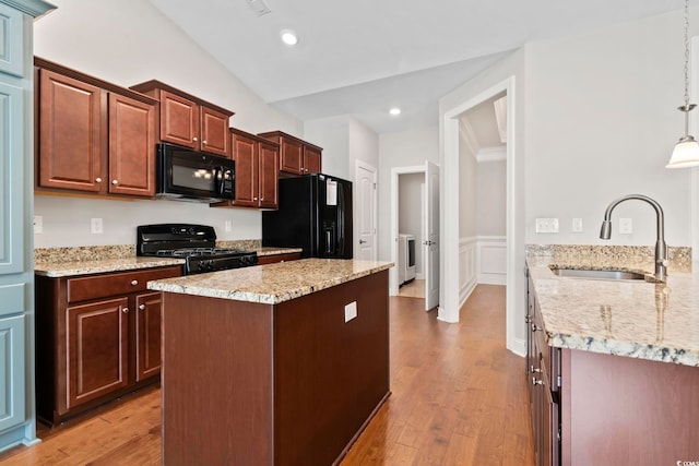 kitchen with black appliances, a sink, light wood-style floors, a wainscoted wall, and light stone countertops