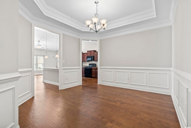 unfurnished dining area featuring a chandelier, crown molding, dark wood finished floors, wainscoting, and a tray ceiling