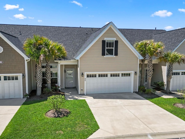 traditional home with driveway, a front lawn, a shingled roof, and an attached garage