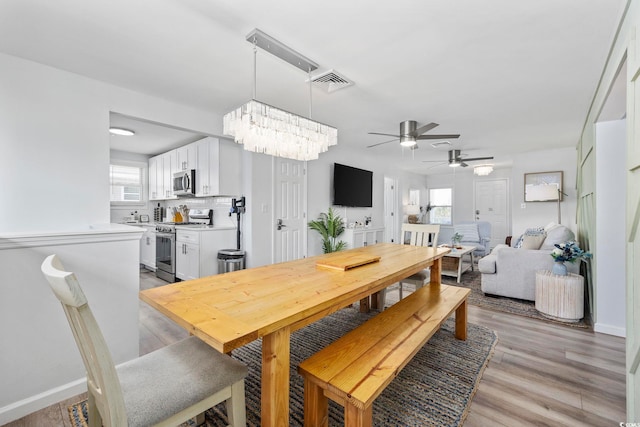 dining room featuring visible vents, light wood finished floors, ceiling fan with notable chandelier, and baseboards