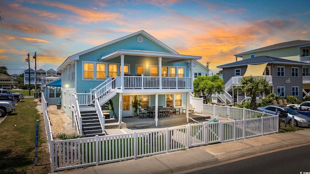 back of house at dusk featuring covered porch, outdoor dining area, a fenced backyard, a patio, and stairs