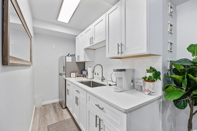kitchen with decorative backsplash, freestanding refrigerator, light countertops, a sink, and light wood finished floors