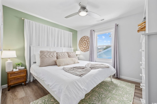 bedroom with baseboards, ceiling fan, wood finished floors, and visible vents