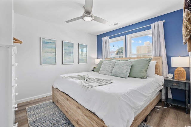 bedroom with baseboards, ceiling fan, wood finished floors, and visible vents