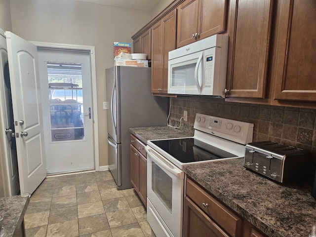 kitchen featuring dark stone countertops, stone finish flooring, baseboards, white appliances, and backsplash