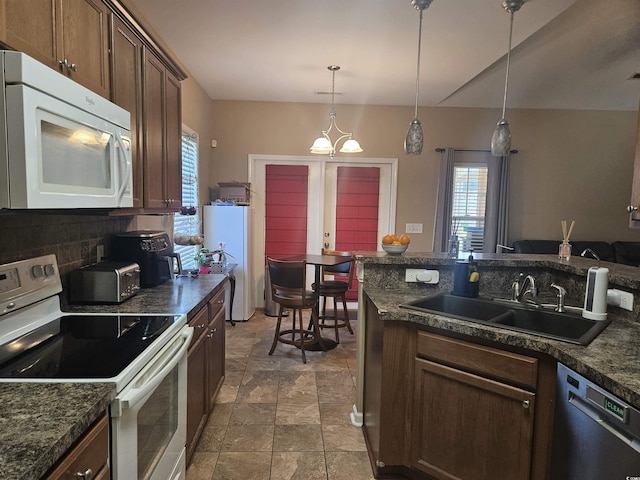 kitchen featuring white appliances, stone finish flooring, dark countertops, backsplash, and a sink
