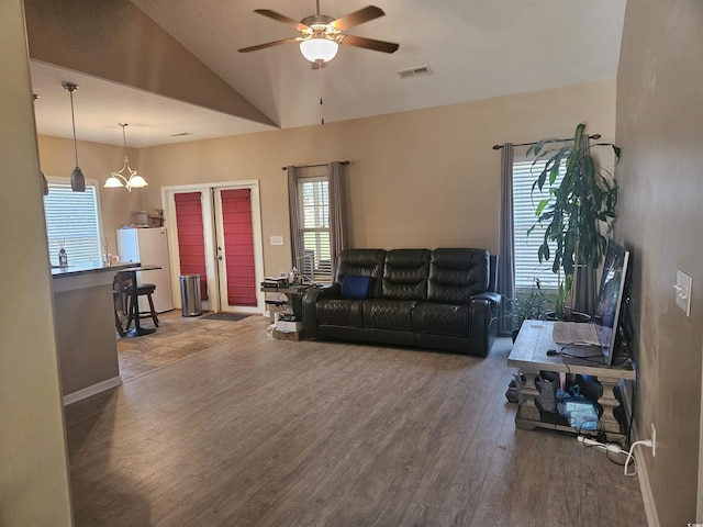 living room with wood finished floors, vaulted ceiling, ceiling fan with notable chandelier, baseboards, and visible vents