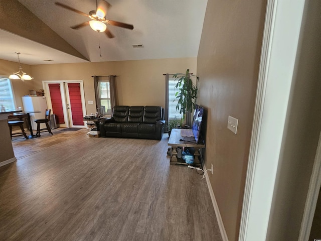 living room featuring lofted ceiling, visible vents, baseboards, wood finished floors, and ceiling fan with notable chandelier