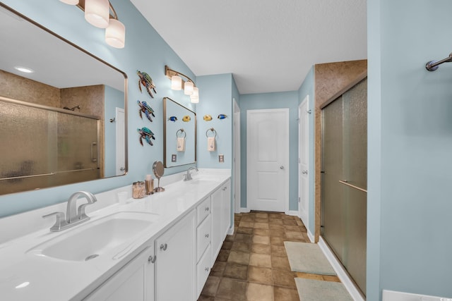 full bath with a stall shower, double vanity, a textured ceiling, baseboards, and stone finish flooring