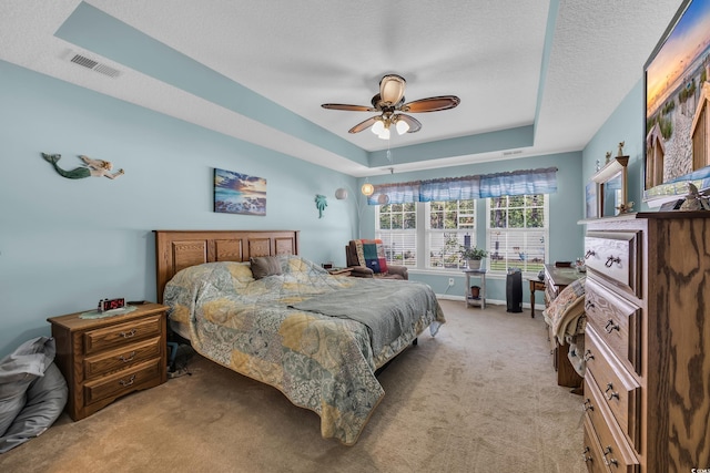 bedroom featuring light colored carpet, a tray ceiling, a textured ceiling, and ceiling fan