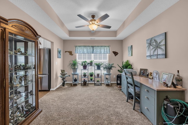 office space with ceiling fan, light colored carpet, a raised ceiling, and baseboards