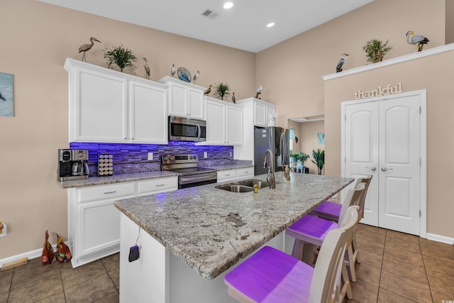 kitchen featuring stainless steel appliances, a sink, a center island with sink, white cabinets, and recessed lighting