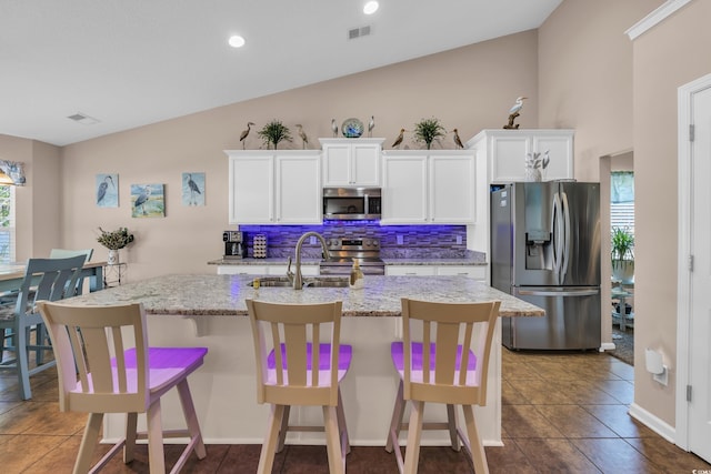kitchen featuring stainless steel appliances, a sink, an island with sink, white cabinetry, and vaulted ceiling