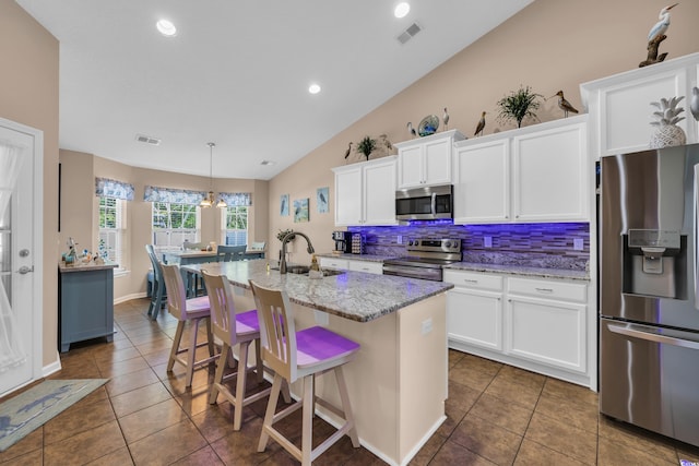 kitchen with appliances with stainless steel finishes, a sink, tile patterned flooring, lofted ceiling, and tasteful backsplash