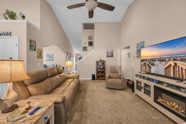 carpeted living area with high vaulted ceiling, a ceiling fan, arched walkways, baseboards, and stairs