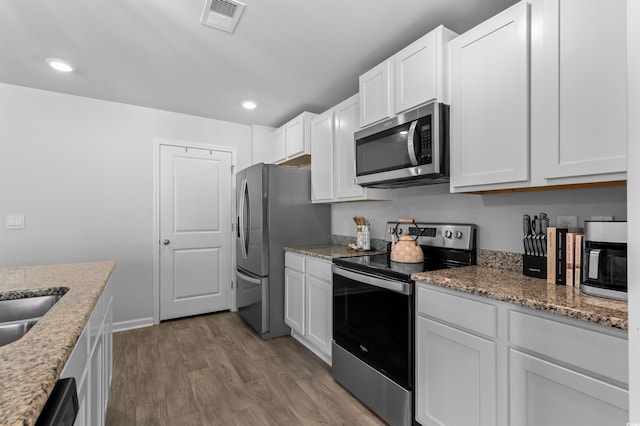 kitchen with visible vents, wood finished floors, white cabinets, light stone counters, and stainless steel appliances
