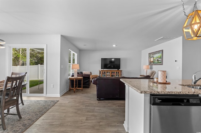 kitchen featuring stainless steel dishwasher, light stone counters, a wealth of natural light, and wood finished floors